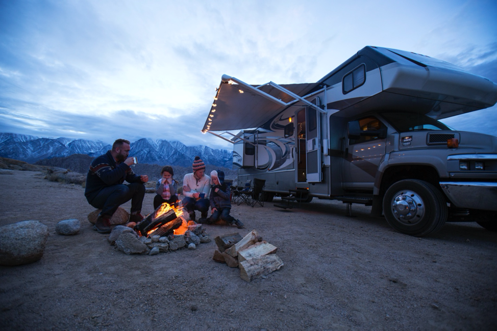 A family around a campfire in front of a class C motorhome. 