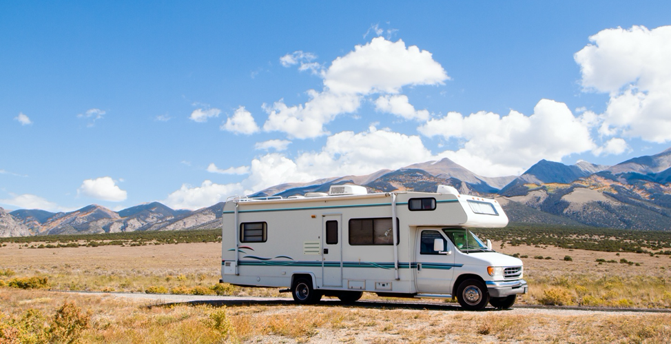 A class C motorhome driving with mountains in the background. 