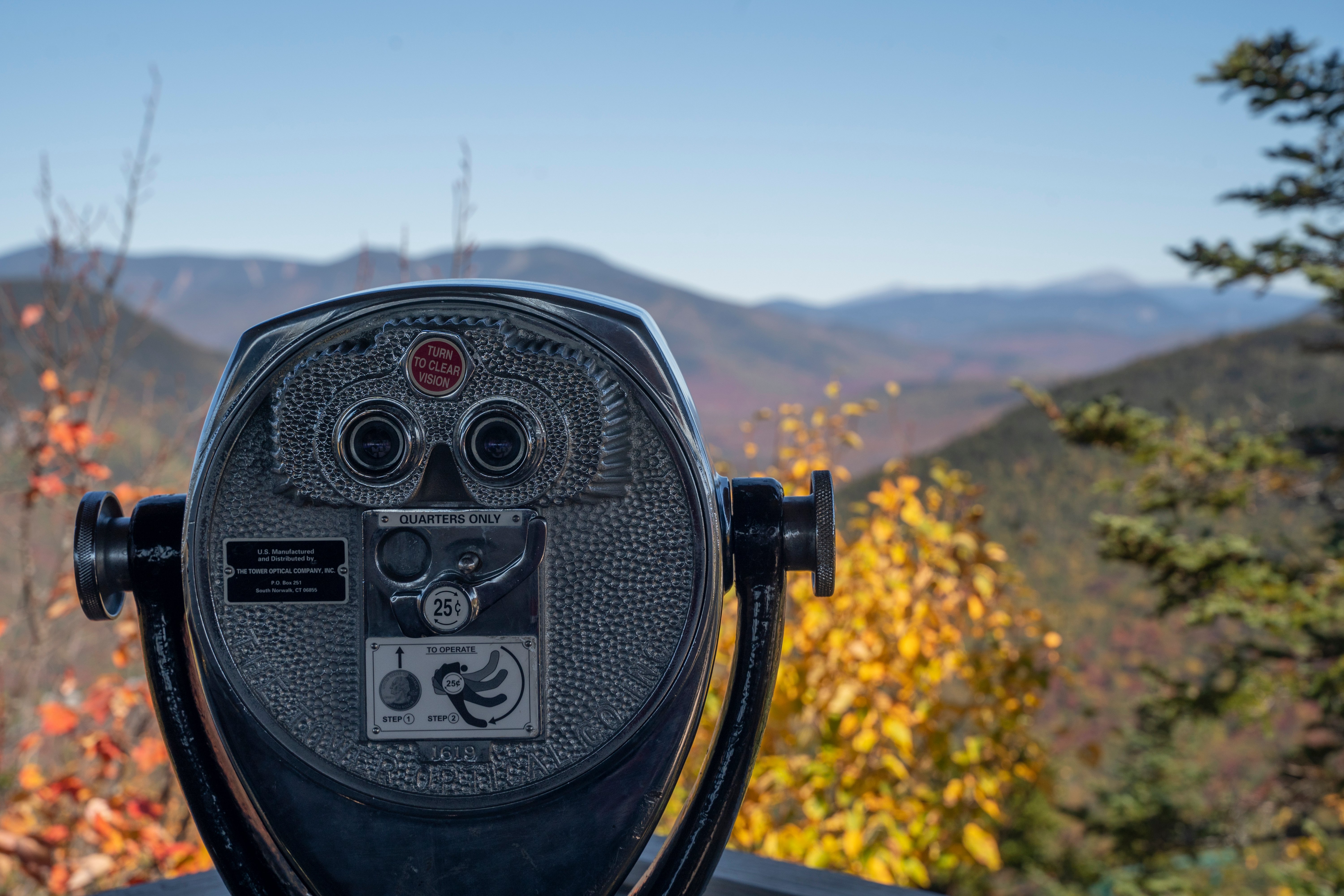 A photo of binoculars overlooking mountains with fall leaves. 