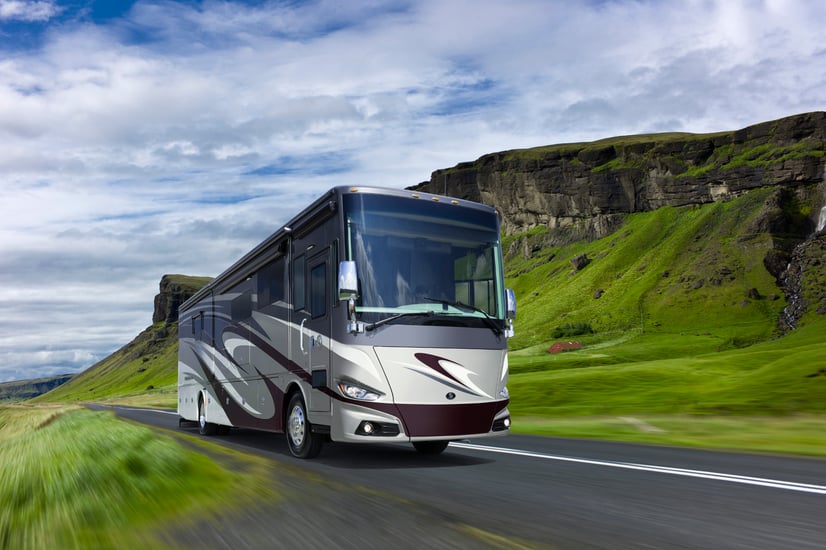 A 2018 Tiffin Phaeton driving down the road with lush green scenery behind. 