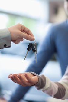 Salesman holding keys over the hand of a customer in a car-shop