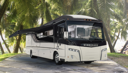 A class A Winnebago motorhome with tropical palm trees behind.