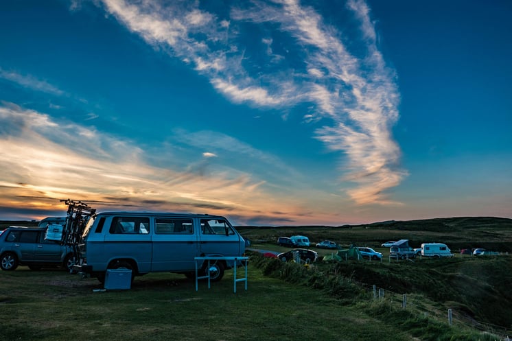 Group of camper vans parked in an open, hilly field at dawn