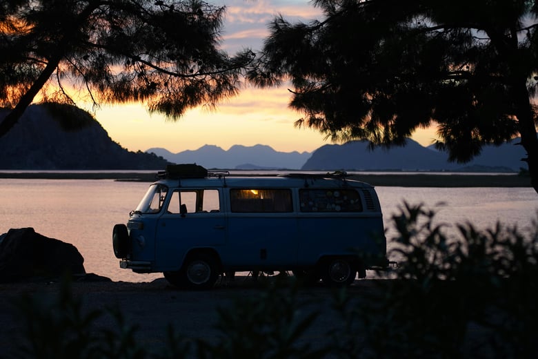 Older model Class B RV parked by a large lake in a forest at dusk