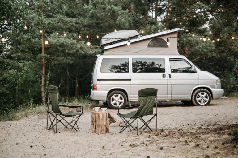 Class B RV with a pop-up section sits at a sandy campsite in the forest