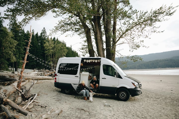Young couple and their dog sit by their Class B RV on the beach