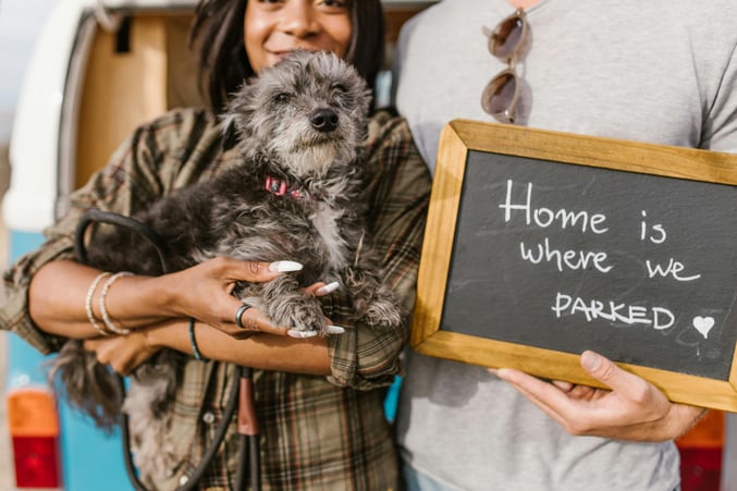 Couple with dog poses next to a chalk sign reading "Home is where we parked"