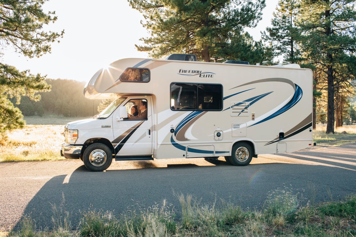 Couple driving in an RV campers on a sunny day with trees around them