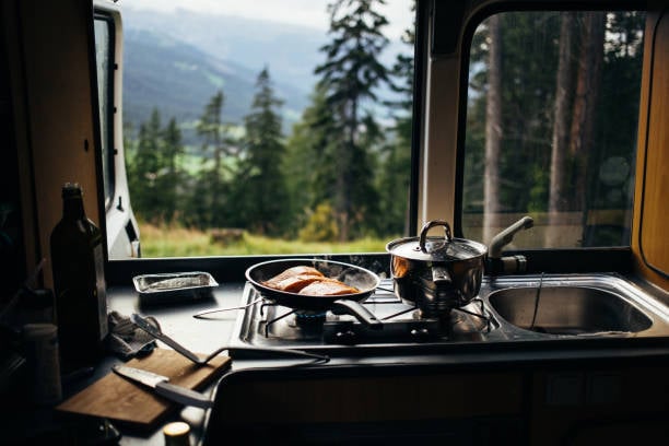 Meat cooks on an RV's stovetop that looks over mountains