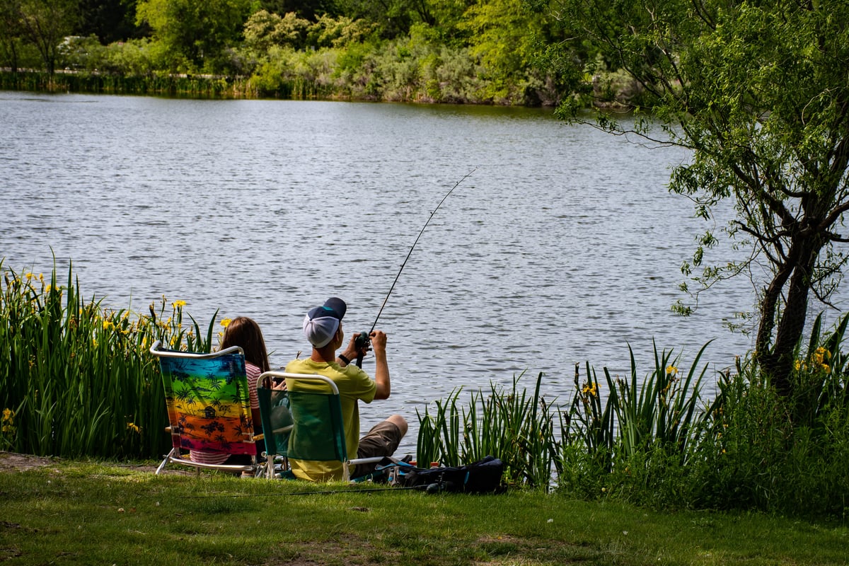 two people sitting on the edge of a lake fishing