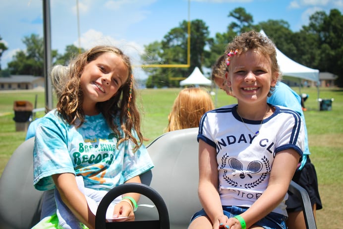 two_smiling_children_sit_in_golf_cart_on_football_field
