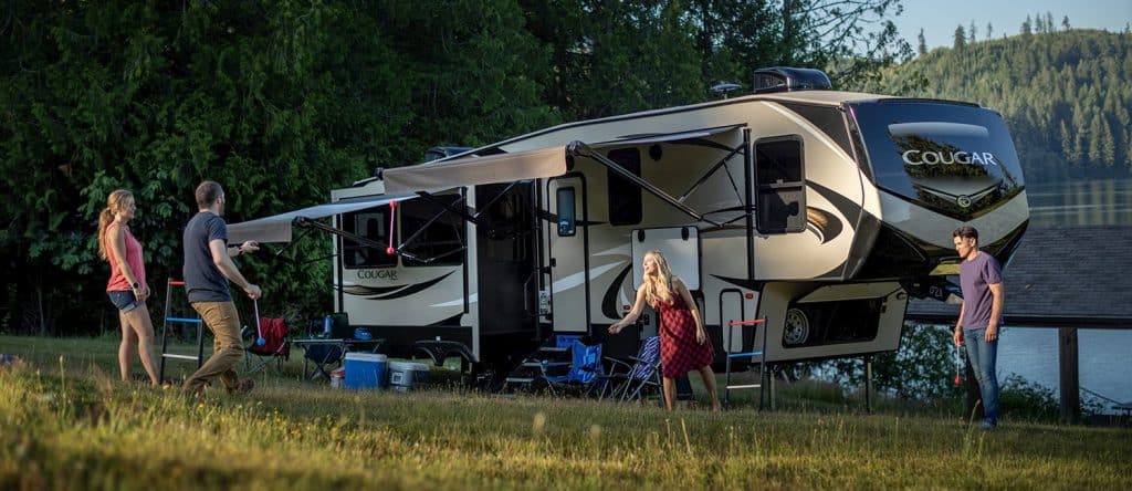 The exterior of a cougar fifth wheel while a family plays outside together