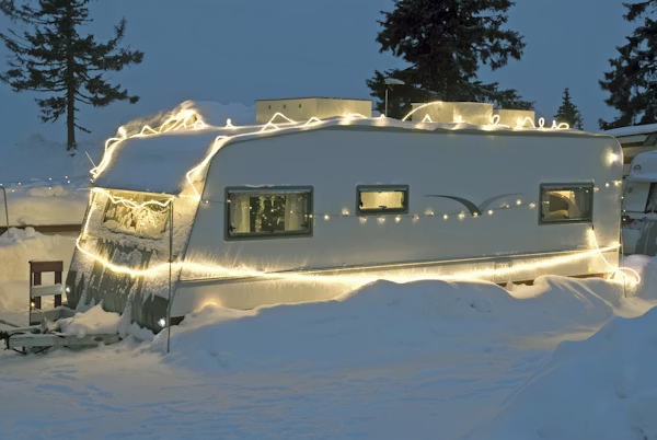 festive lights decorate a camper in the snow